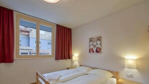Une chambre à coucher avec un lit double, deux tables de chevet, une fenêtre avec des rideaux et un luminaire fixé au mur.