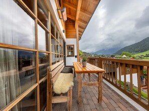 A wooden balcony with a bench and table, overlooking a mountainous landscape.