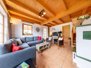 A cozy living room with a sectional sofa, a coffee table, and a TV. There are windows with curtains, a fireplace, and a kitchen area visible. - Stylish Ten-Person Alpine Chalet (Wald-Königsleiten)
