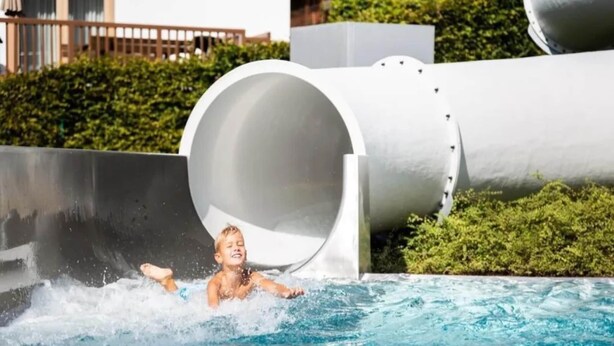 A water slide with a person at the bottom, water flowing down, and a building in the background.
