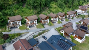 A residential area with multiple houses, a winding road, and dense forest in the background.