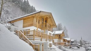A wooden chalet with a balcony, set in a snowy landscape.