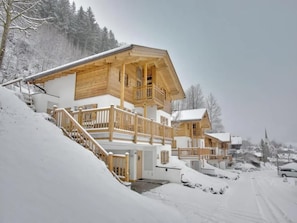 A wooden chalet with a balcony, set in a snowy landscape.