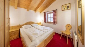 A bedroom with a wooden ceiling, a bed, a chair, a window with curtains, and a radiator.