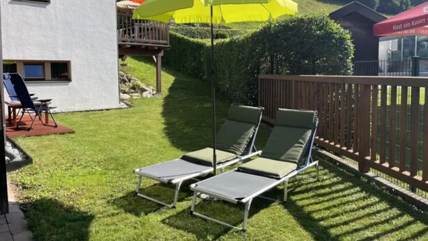 A backyard with two lounge chairs, a yellow umbrella, and a wooden deck. - Zirbenholz Alpine Maisonette Stay (Wald-Königsleiten)
