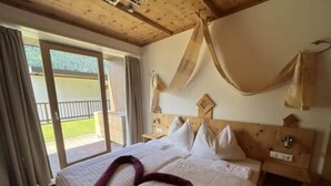 A hotel room with a large bed, a wooden headboard, and a view of a balcony. - Zirbenholz Alpine Maisonette Stay (Wald-Königsleiten)