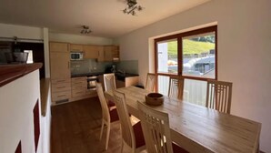 A kitchen with wooden cabinets, a microwave, and a dining area with a table and chairs. - Zirbenholz Alpine Maisonette Stay (Wald-Königsleiten)
