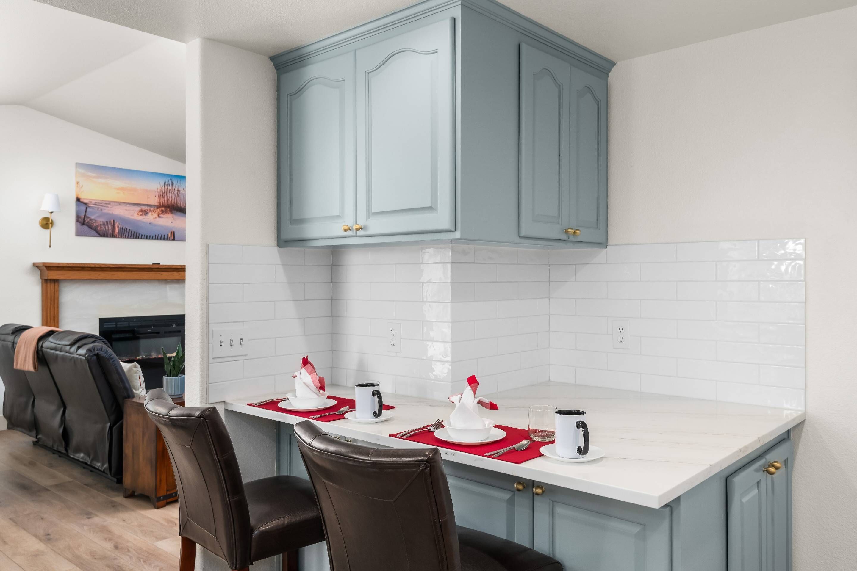 Una cocina moderna con armarios azul claro, encimeras blancas y un comedor con un mantel individual rojo.