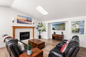 A spacious living room with a fireplace, leather sofas, a coffee table, and a large window with a view of a coastal landscape. - New listing! Beautiful 3 bedroom 3 bath, near lakes, ocean, and dunes, pet friendly, large lot, bbq (Florence)
