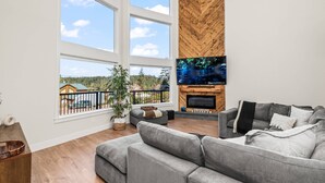 Ein modernes Wohnzimmer mit einem grauen Sofa, einem Kamin und einem großen Fernsehbildschirm.