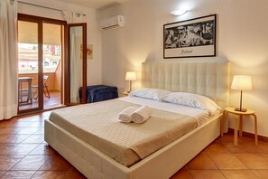 A hotel room with a bed, two bedside lamps, a framed artwork on the wall, and a balcony with a chair.