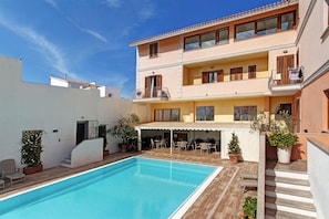 A two-story building with a swimming pool, outdoor seating, and potted plants.