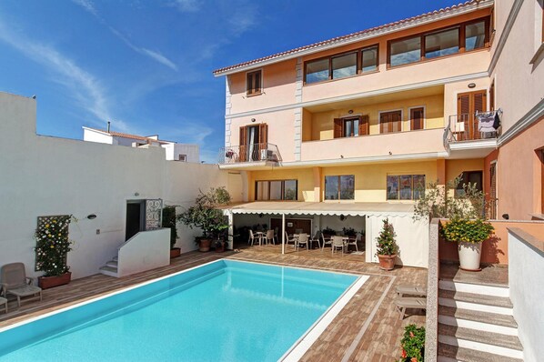 A two-story building with a swimming pool, outdoor seating, and potted plants.