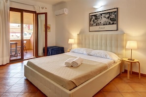 A hotel room with a bed, two bedside lamps, a framed artwork on the wall, and a balcony with a chair. - Apartment in Santa Teresa Gallura (Santa Teresa di Gallura)