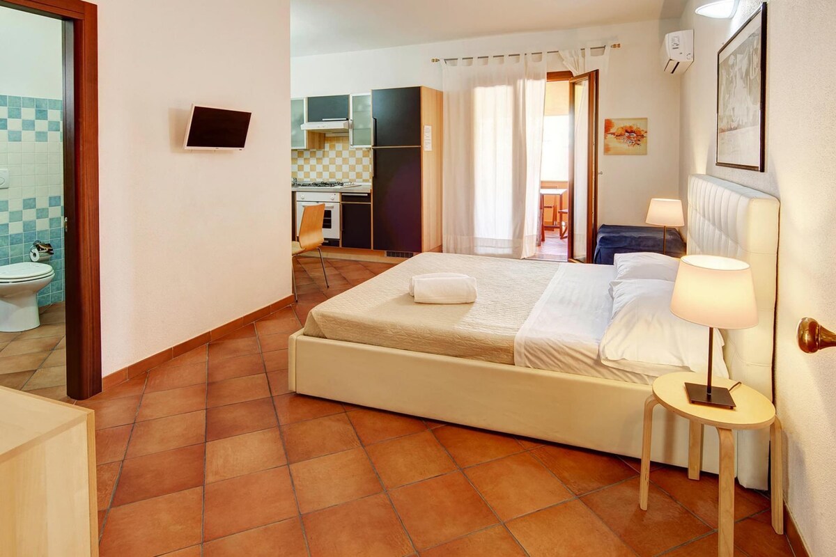 Une chambre d’hôtel comprenant un lit, une table de chevet, une lampe et donnant sur la cuisine et la salle de bain.