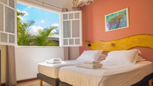 A double bed with white linens, a wooden headboard, and a window with a view of greenery.