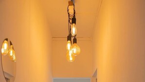 A hallway with light fixtures and mirrors on the walls, leading to a room with a window and a door.