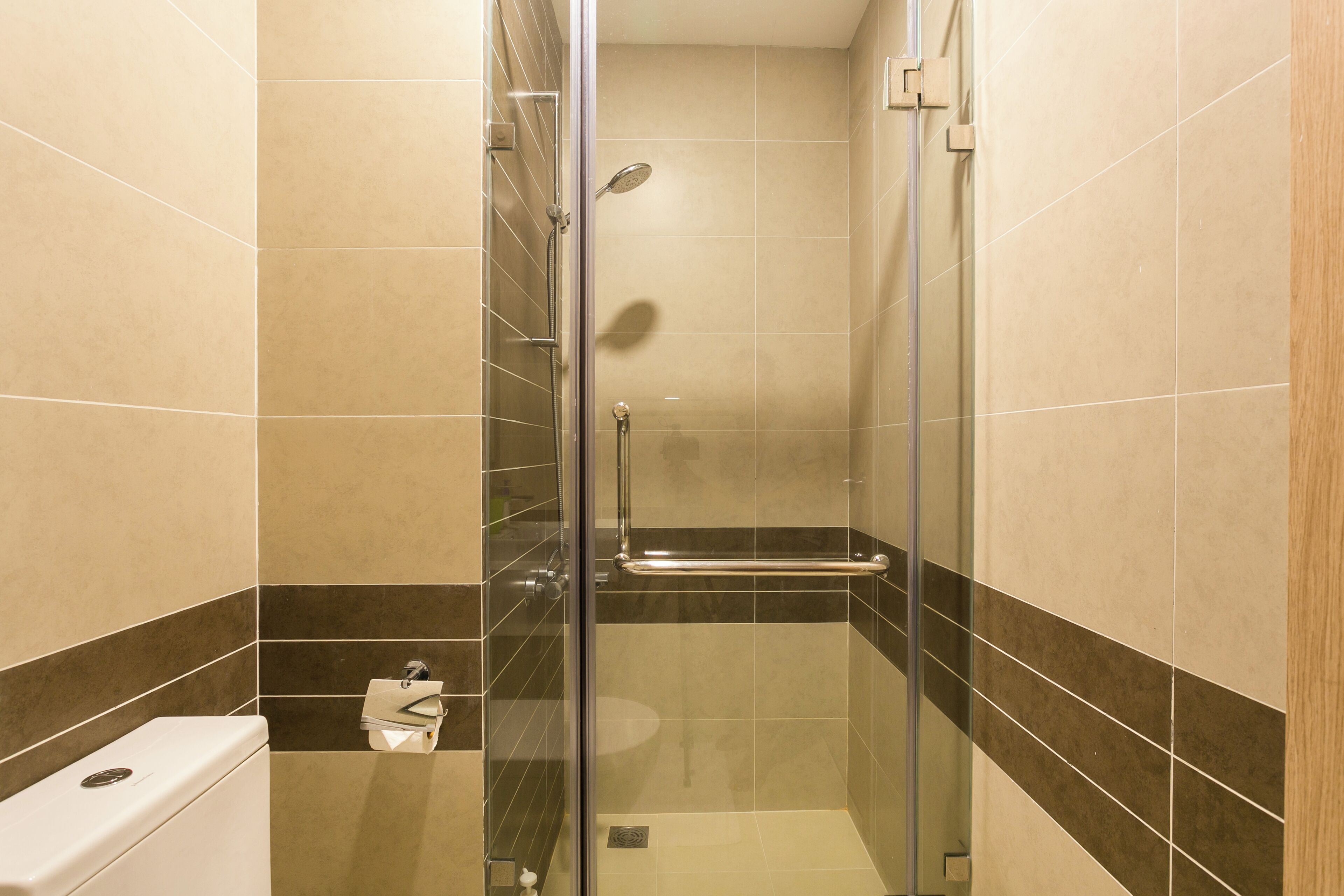 A glass-enclosed shower stall with a handheld showerhead, a glass door, and a small shelf.