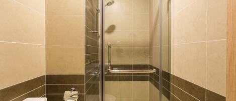 A glass-enclosed shower stall with a handheld showerhead, a glass door, and a small shelf.