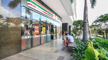 A 7-Eleven store with a modern glass facade, located in a commercial area with palm trees and a tiled walkway.
