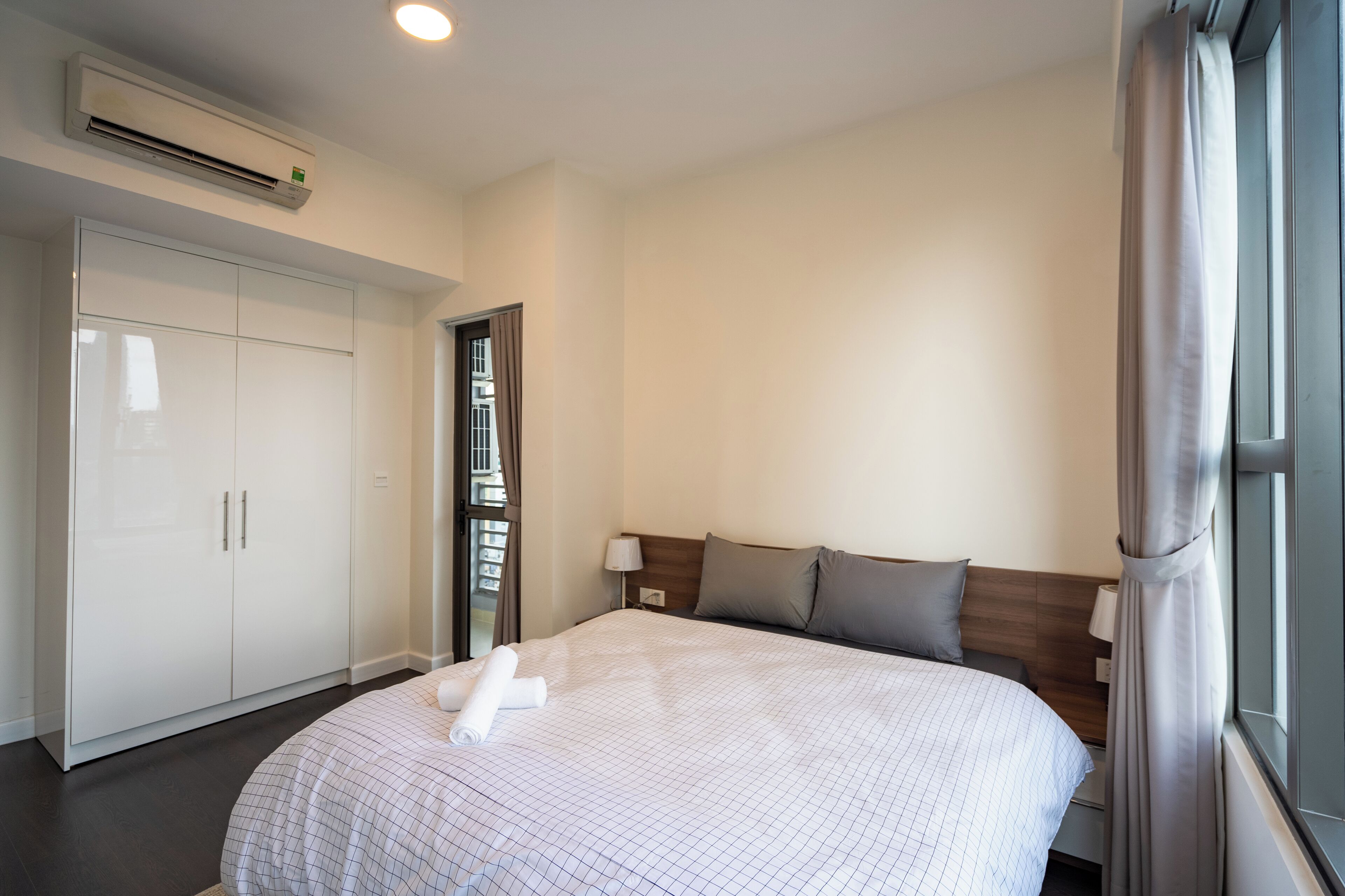 Ein Hotelzimmer mit einem großen Bett, einem Kleiderschrank, einem Fenster mit Vorhängen und einer Klimaanlage.