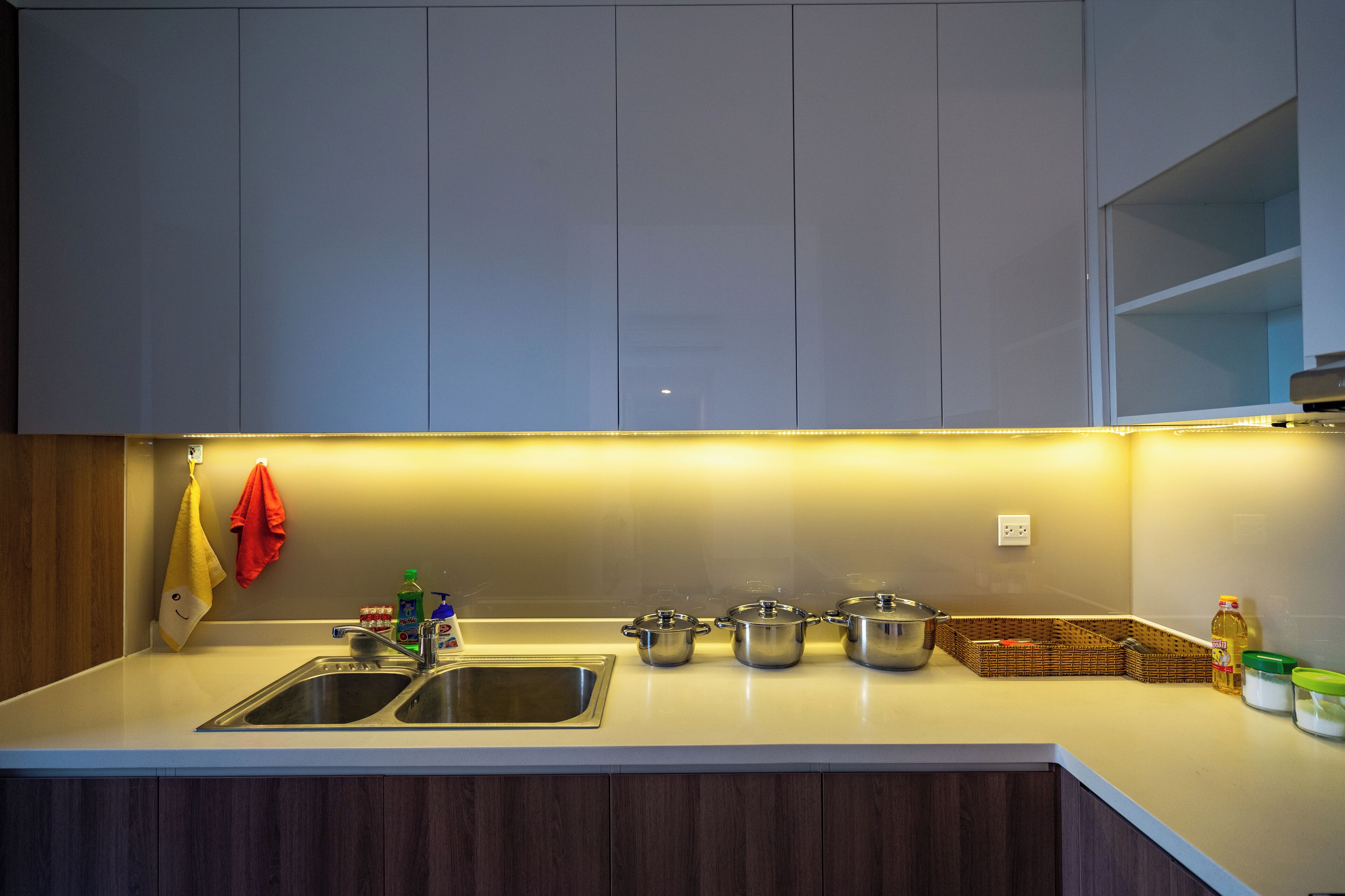 A modern kitchen with a double sink, stainless steel pots, a basket, and a bottle of dish soap.