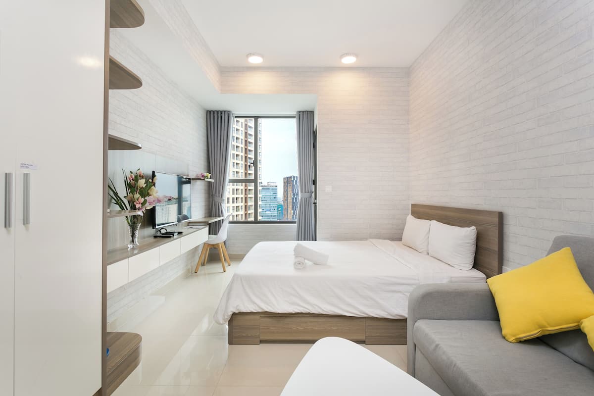 Une chambre d’hôtel moderne équipée d’un lit, d’un bureau, d’un canapé et d’une grande fenêtre donnant sur la ville.