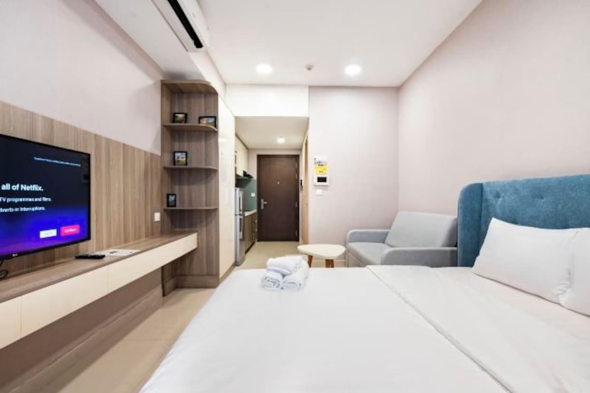 Una camera d'albergo con un letto, una televisione su una mensola di legno, un tavolino e un divano.