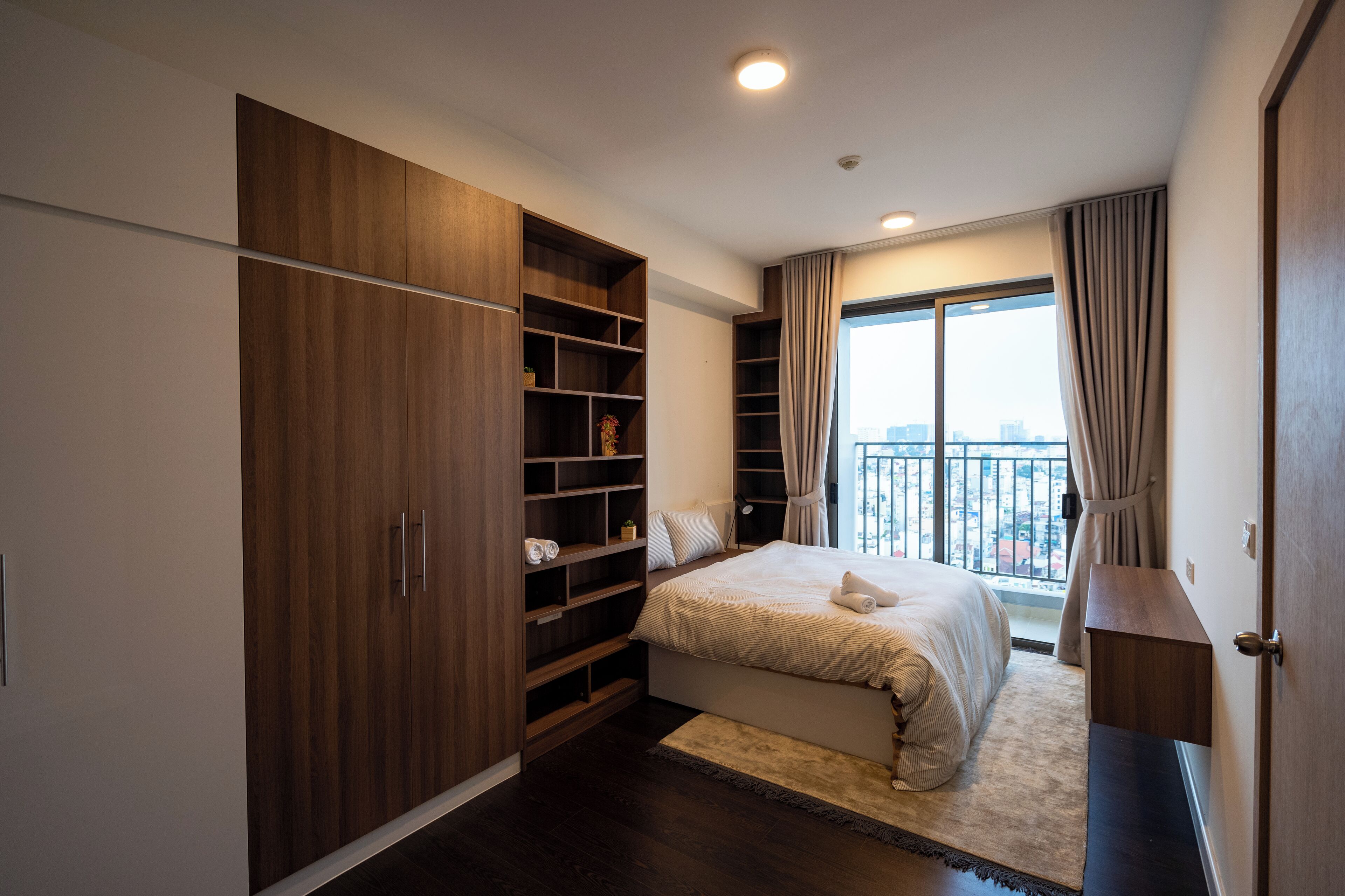 Une chambre avec une grande armoire, un lit, une fenêtre avec des rideaux et une vue sur la ville.