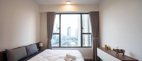 Habitación de hotel moderna con una cama grande, una mesita de noche, un escritorio y vistas de la ciudad a través de un ventanal amplio.