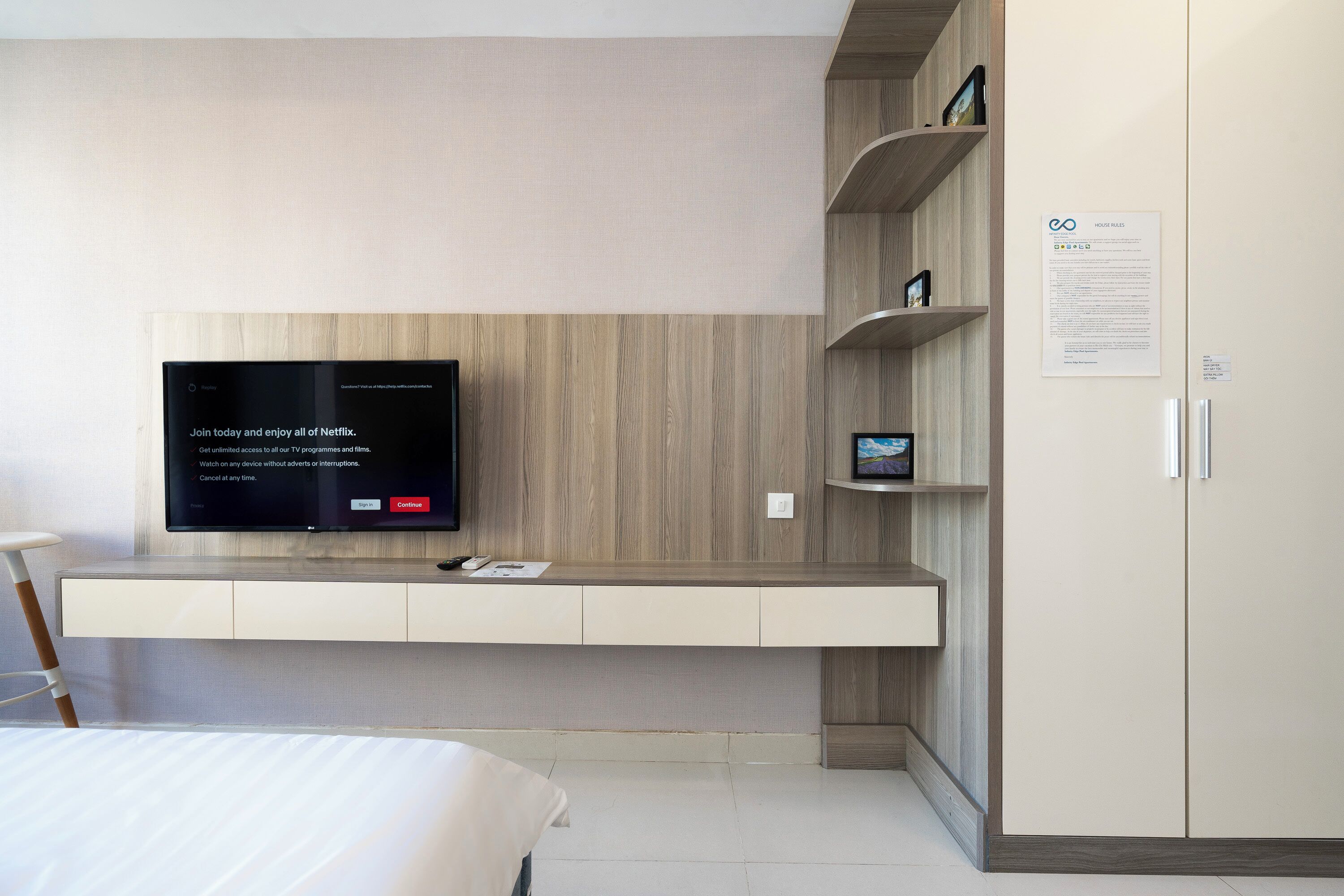 A modern hotel room with a mounted TV, built-in shelving, a wardrobe, and a bed.