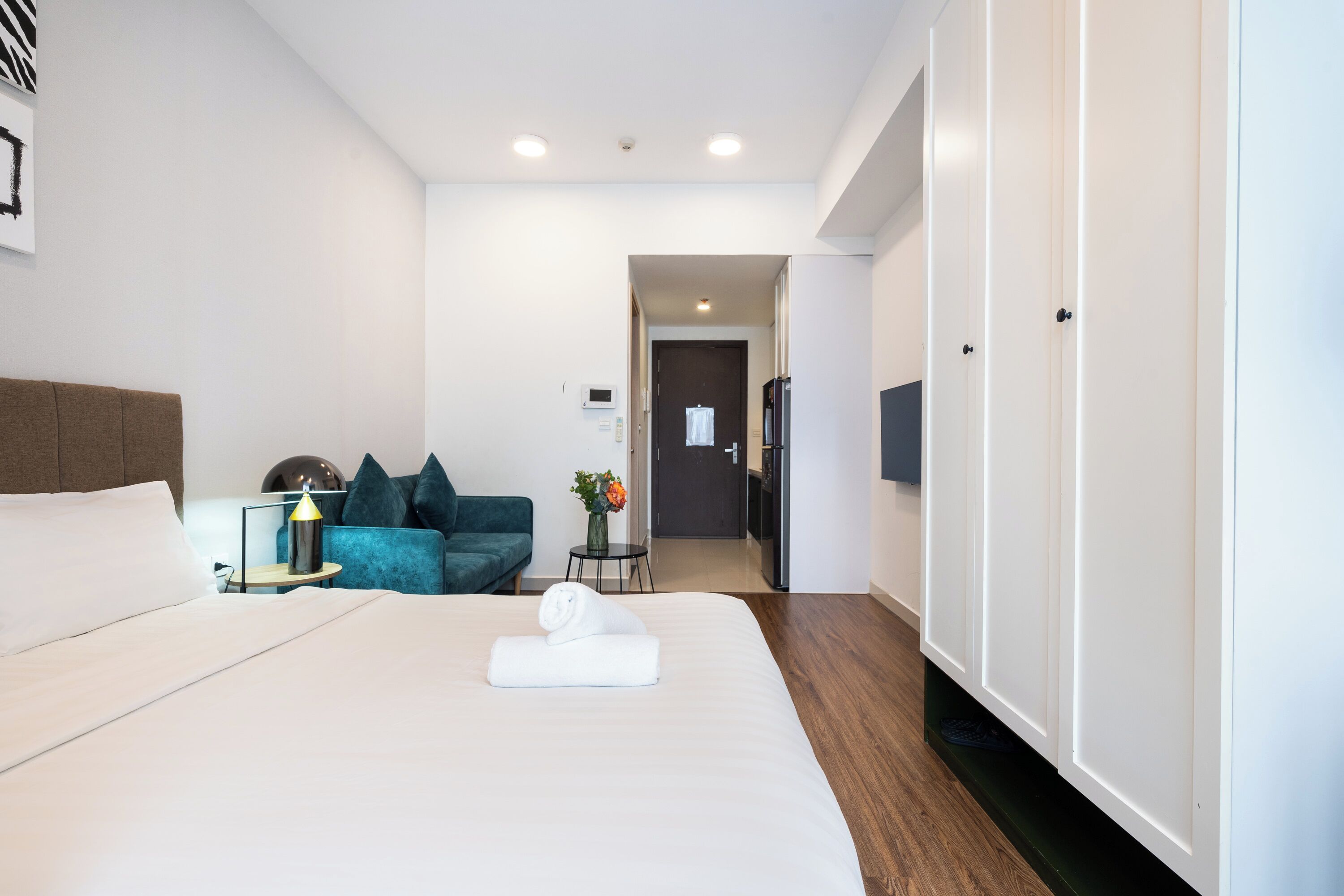 A hotel room with a large bed, a sofa, a small table with a lamp, and a wardrobe.