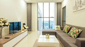 Ein modernes Wohnzimmer mit einem Flachbildfernseher, einer Couch mit tropischen Kissen, einem Couchtisch und einem großen Fenster mit Blick auf die Stadt.