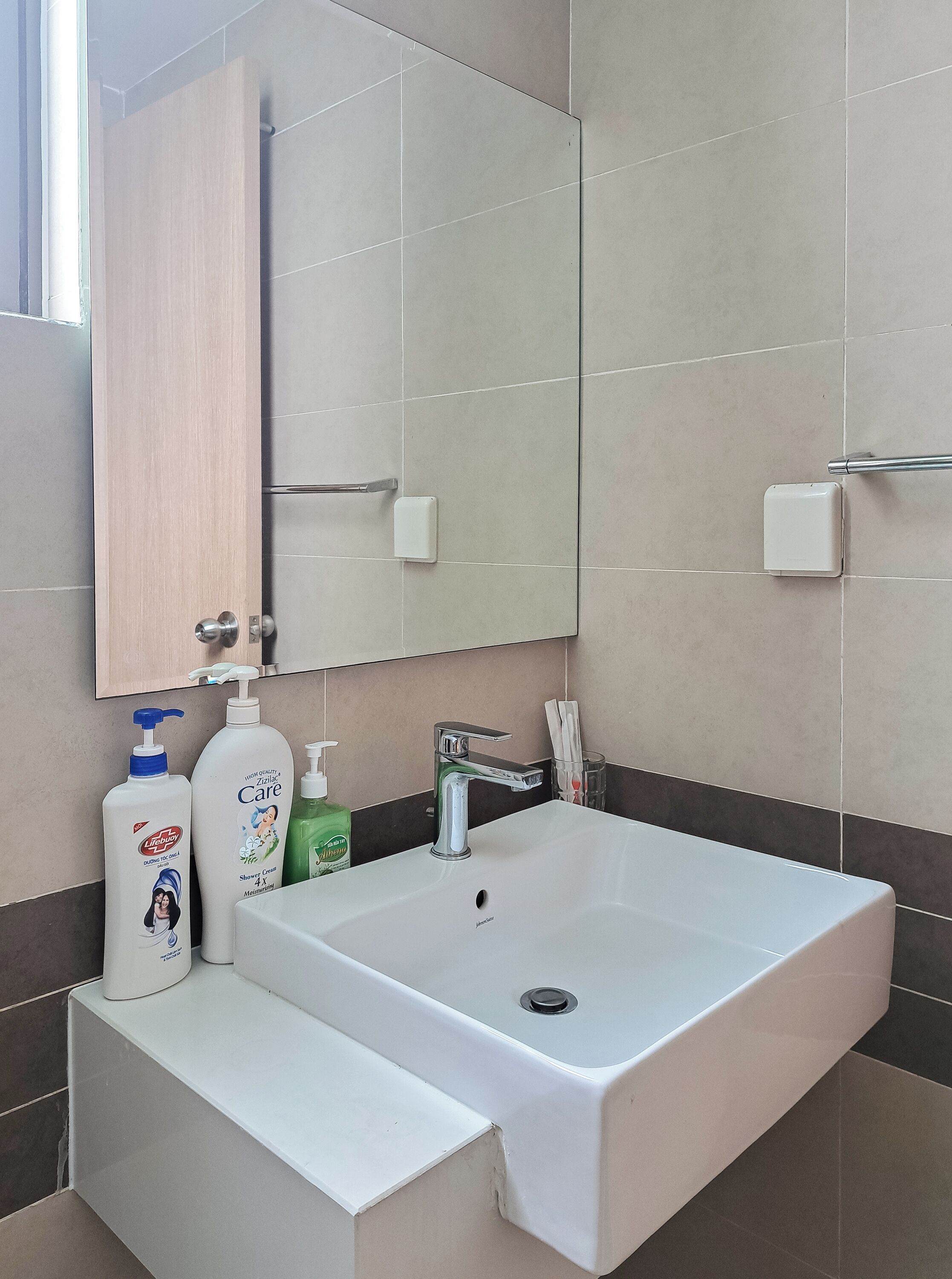 Et badeværelse med en hvid vask, et spejl og toiletartikler.