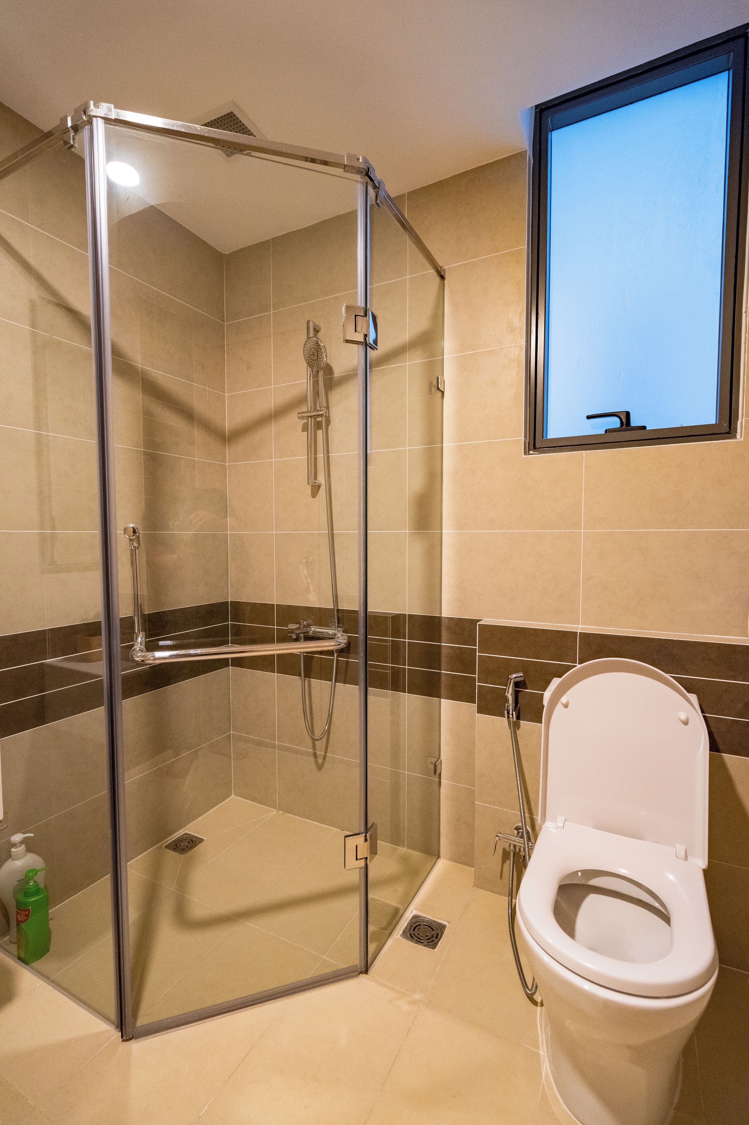 Une salle de bain avec une douche à parois de verre, des toilettes et une fenêtre au-dessus du lavabo.