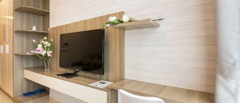 A modern hotel room with a wooden TV stand, a flat-screen TV, a white chair, and a vase with flowers.
