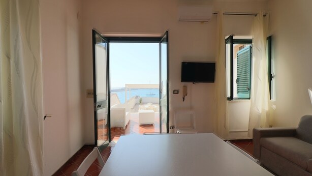 Ein Zimmer mit Bett, einer Couch und einem Fernseher. Es gibt einen Balkon mit Meerblick.