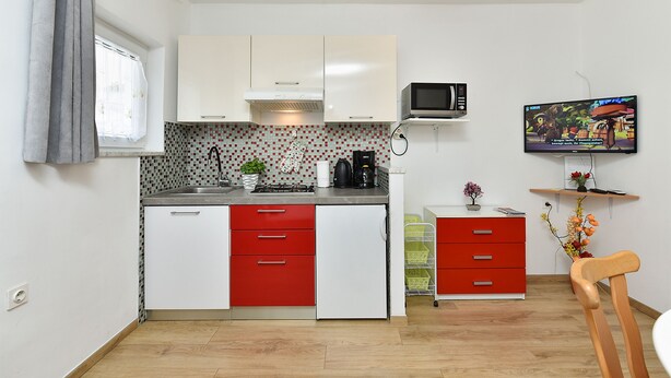 Una cocina funcional con armarios blancos y rojos, un microondas y un televisor pequeño en un estante.