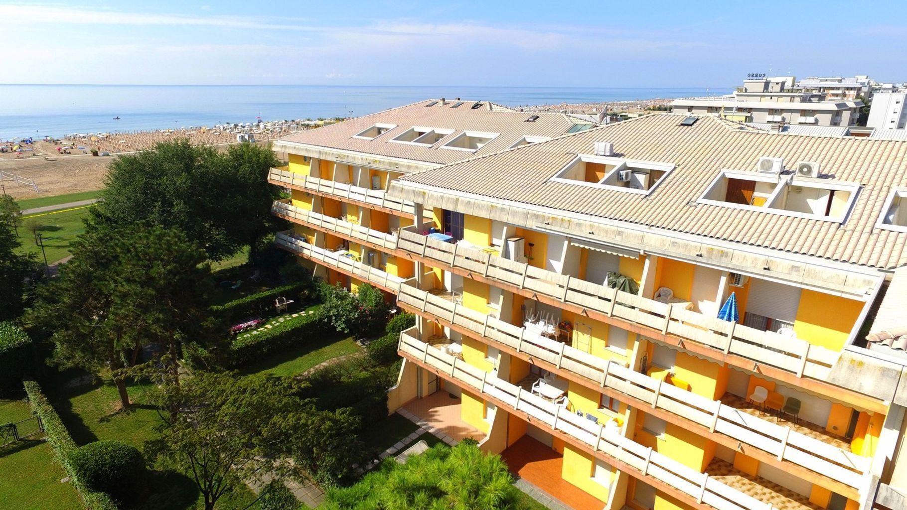 Ett hotell med flera våningar, balkonger, en trädgård och utsikt över stranden och havet.
