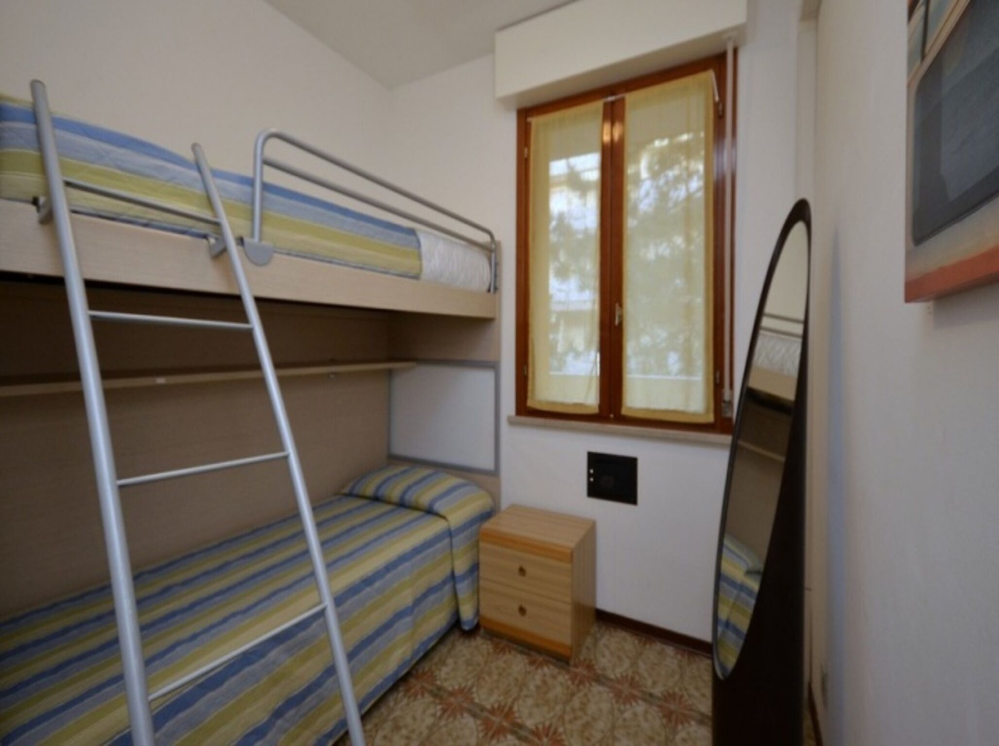 Une petite pièce avec des lits superposés, une fenêtre avec des rideaux, une armoire en bois et un miroir.