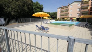 A swimming pool area with sun umbrellas, lounge chairs, and a fenced poolside. - Comfy flat in Rosolina with shared pool (Rosolina Mare)