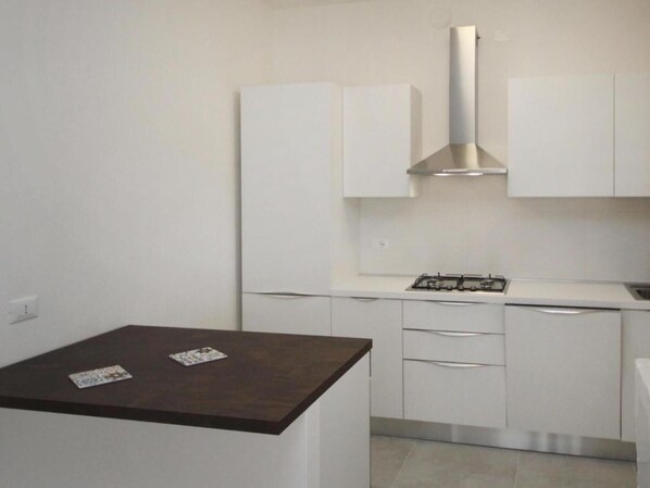 A modern kitchen with white cabinetry, a gas stove, and a dark wooden table.