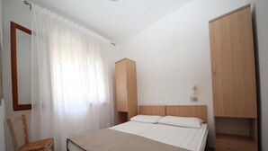 A bedroom with a bed, a wooden wardrobe, a chair, and a mirror. - Comfortable beachside apartment in Rosolina (Rosolina Mare)