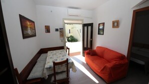 A small, well-lit room with a bed, a red sofa, and a dining table with chairs. There are several framed pictures on the walls. - Cozy apartment close to the beach (Rosolina Mare)