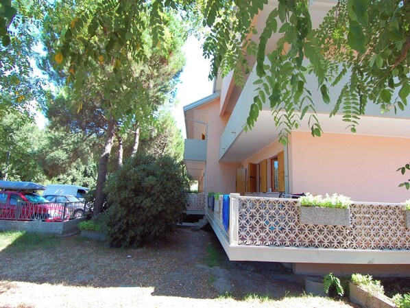 A two-story building with a balcony, a covered outdoor seating area, and a parking area with cars.
