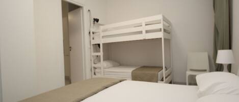 A room with a bunk bed, a bedside table with a lamp, and a chair.