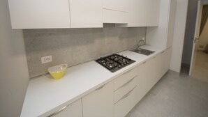 A modern kitchen with white cabinets, a gas stove, and a sink. - Modern apartment near the beach (Rosolina Mare)