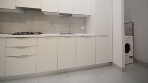 A modern kitchen with white cabinets, a stainless steel sink, and a built-in washing machine. - Modern apartment near the beach (Rosolina Mare)