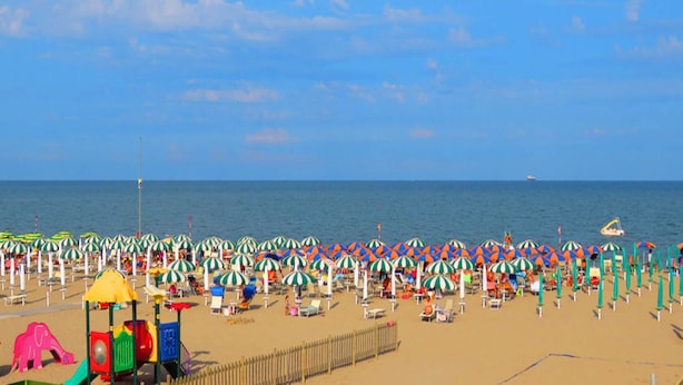 Une plage bordée de rangées de parasols et de chaises longues, une aire de jeux et une clôture.
