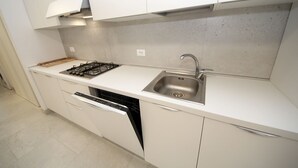 A modern kitchen with white cabinetry, a built-in gas stove, a stainless steel sink, and a dishwasher. - Modern two bedroom apartment near Rosolina beach (Rosolina Mare)
